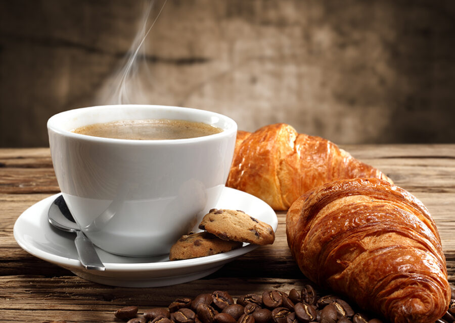 Photo représentant une tasse de café fumante et un croissant.