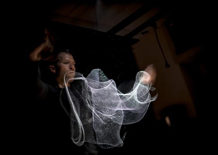 Le comédien-manipulateur met en mouvement de façon invisible un tissu tramé qui prend la lumière comme du métal.