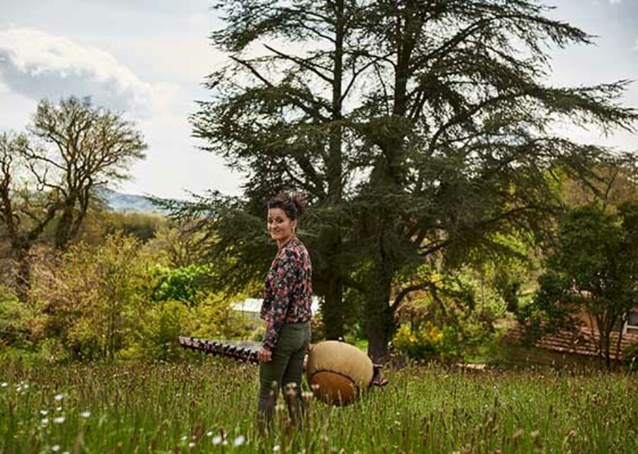 Delphine Noly portant sa kora dans un champ avec de grands arbres au fond.