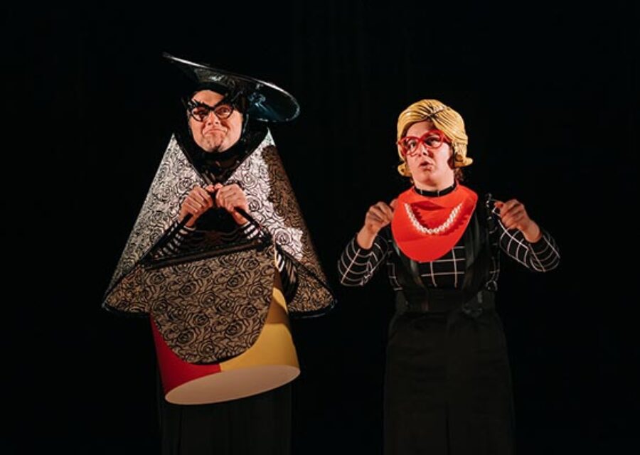 Un comédien portant un costume très géométrique et excentrique (chapeau, cape et sac à main) pour incarner le personnage de la grand-mère. A sa droite une comédienne porte une perruque en plastique jaune, des lunettes rouges et un gros collier de perles blanches pour incarner le personnage de la mère.