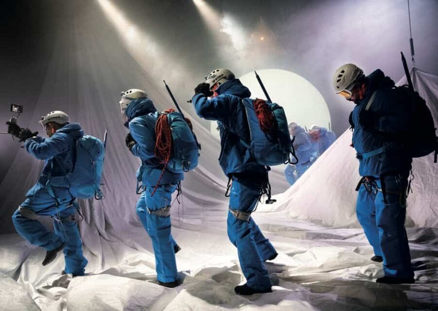 Le décor représente une montagne enneigée et 4 comédiens en tenue bleue d'alpinistes traversent la scène.