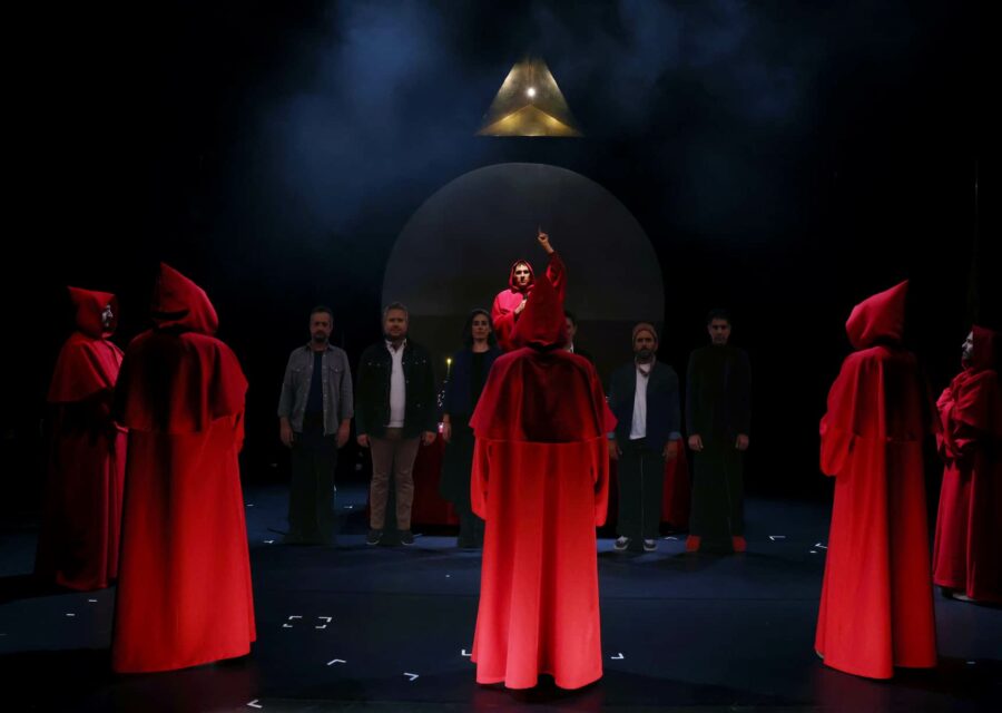 6 personnes de face sont entourées par 6 autres personnes en tenue de moine rouge avec capuchon. Cela ressemble à la cérémonie d'une secte.