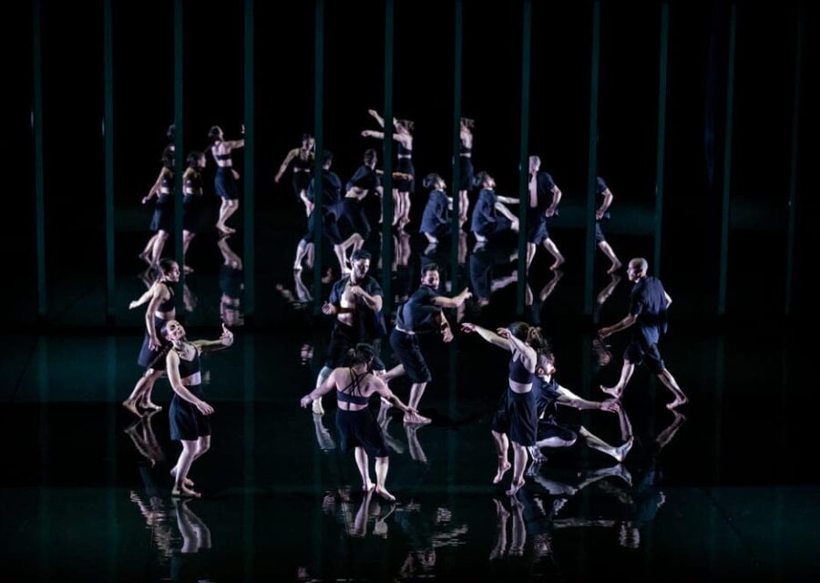 Jeux de reflets des 8 danseurs entre le sol et le décor du fond de scène. Les costumes ont évolué : short et chemise noire pour les hommes, short et brassière noire pour les femmes.