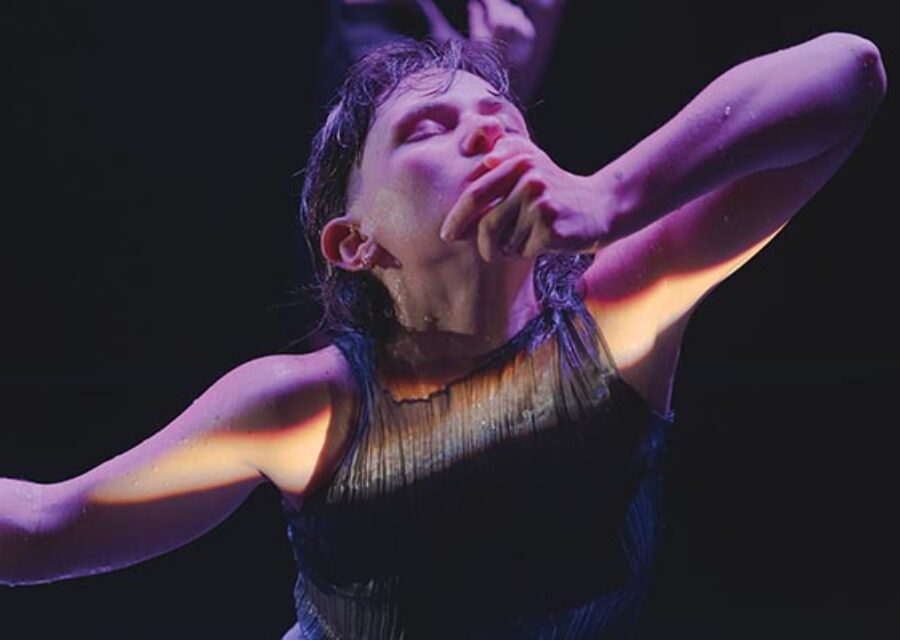 Gros plan sur le haut du corps d'une danseuse éclairé par un trait de lumière suivant la ligne de ses bras. Elle a le visage penché en arrière et les yeux fermés, sa main gauche est posée sur son menton.