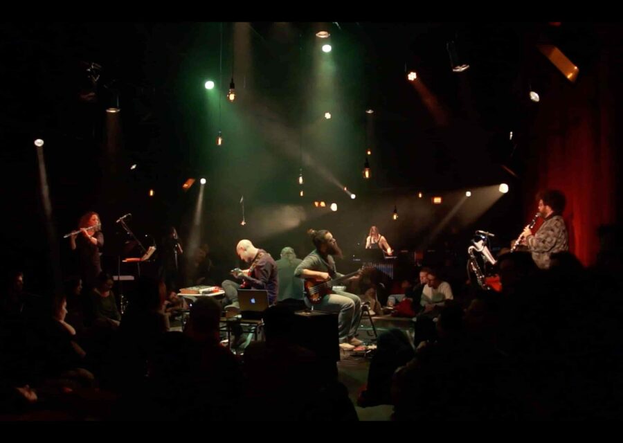 Photo d'une représentation avec les musiciens au centre et les spectateurs autour.