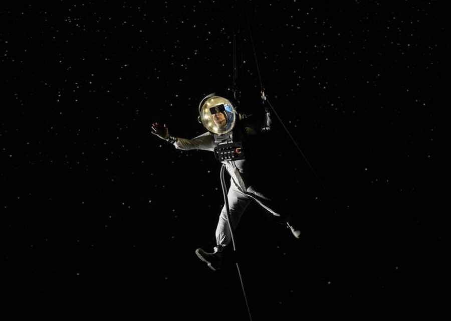 Un comédien dans une tenue ressemblant à celle d'un astronaute semble flotter dans l'espace, comme en apesanteur.