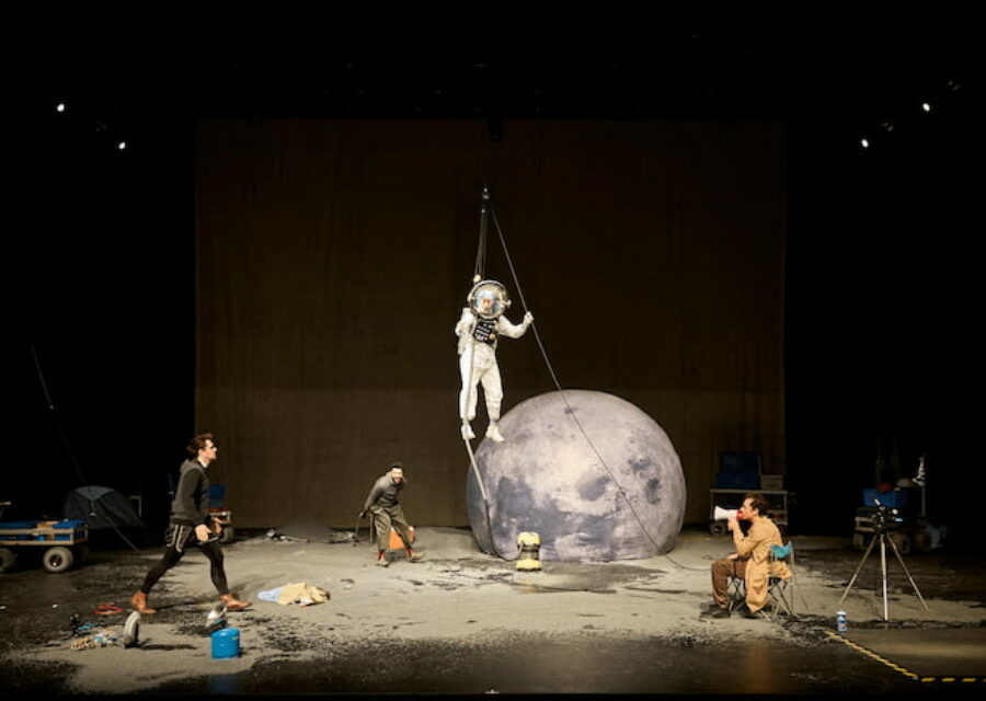 La scène est transformée en studio de cinéma où quatre comédiens simulent un voyage dans l'espace avec une fausse combinaison d'astronaute et une lune gonflable.